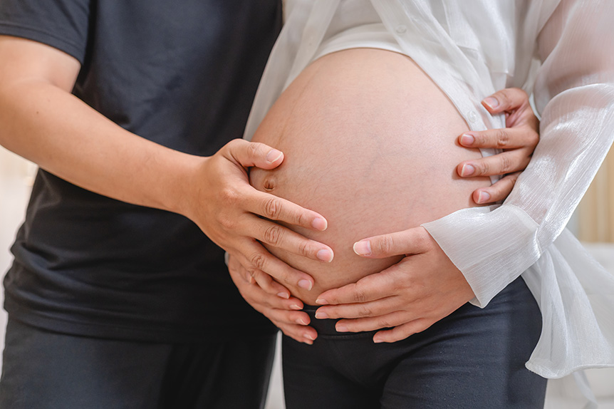 Pregnant woman holding her belly while standing beside her husband