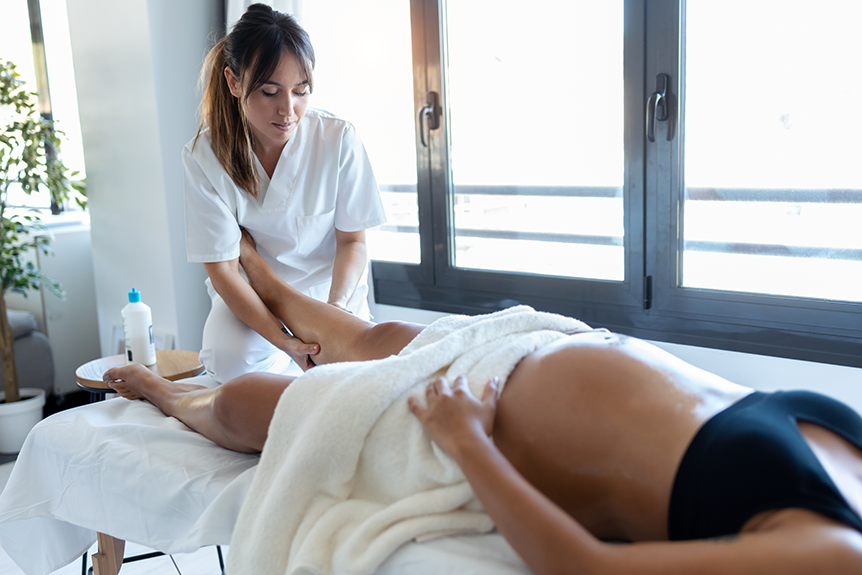 Physiotherapist performing a gentle leg massage on a pregnant woman lying on a treatment table.