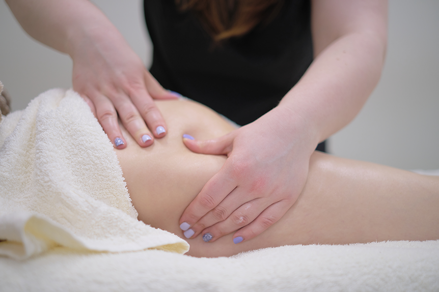 Therapist performing an anti-cellulite leg massage on a woman using firm hand techniques.