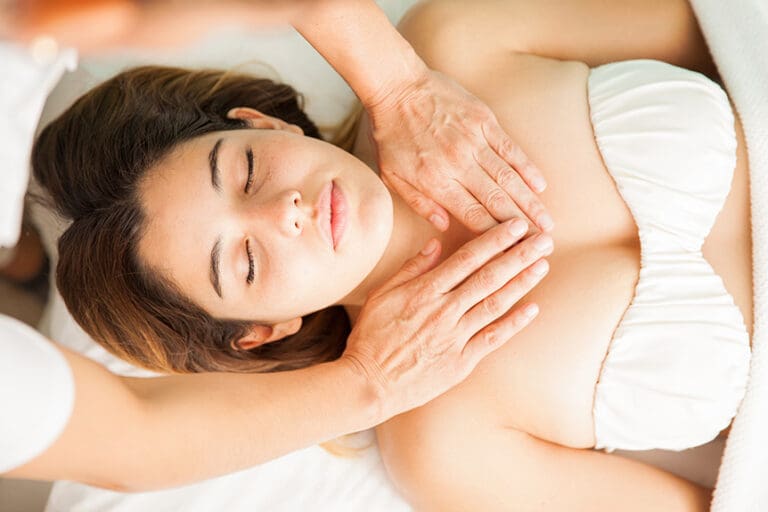 Pregnant woman lying comfortably while a therapist gently massages the upper chest area as part of a safe prenatal relaxation technique.