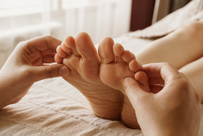 Therapist applying pressure to reflex points on both feet as part of a paid reflexology treatment.