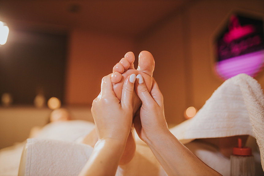 Therapist applying gentle pressure to reflex points on a woman’s feet during a professional reflexology session.