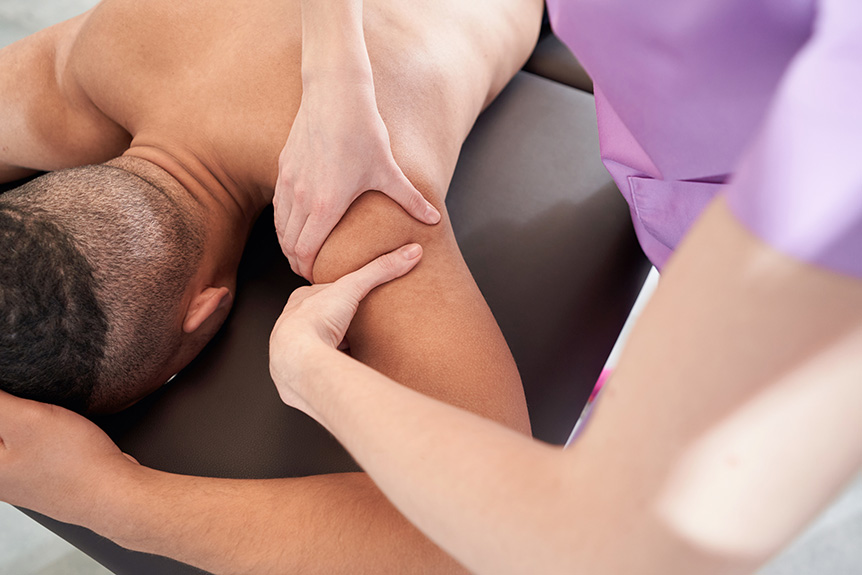 Therapist applying firm pressure to a man’s upper arm during a sports massage to relieve muscle tension and support recovery.