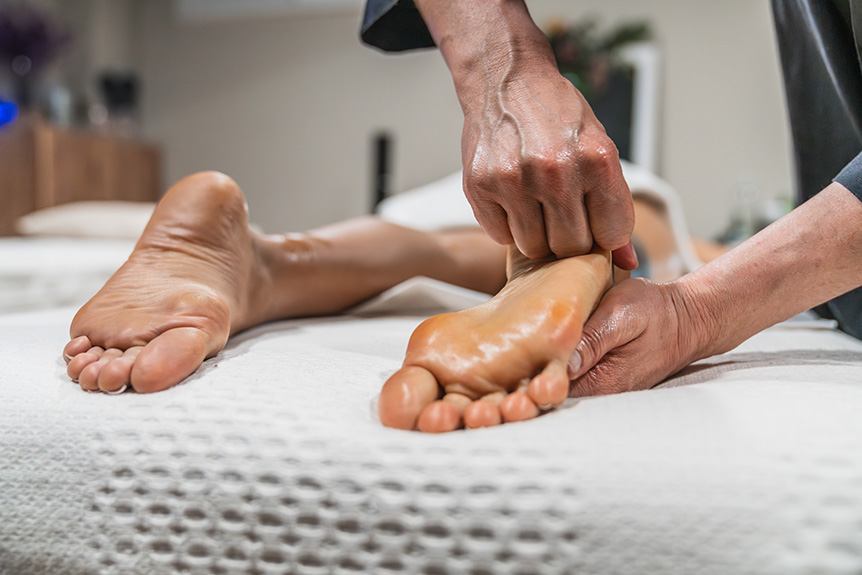 Therapist applying pressure to reflex points on a woman’s foot during a reflexology session aimed at promoting relaxation and overall wellbeing.