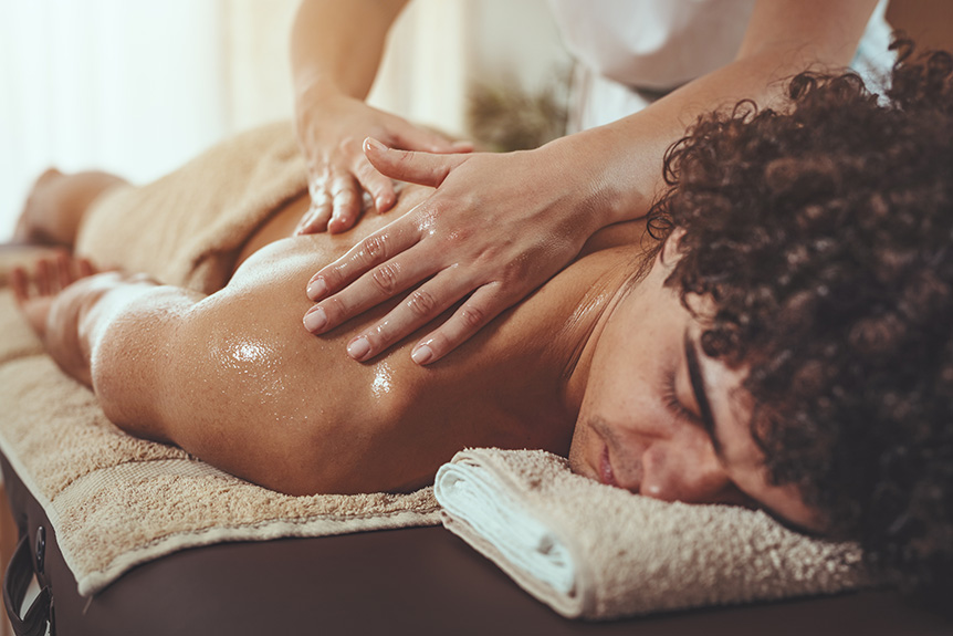 Sports massage therapist applying aromatic massage oil to a client’s back to enhance relaxation, circulation, and post-exercise recovery.