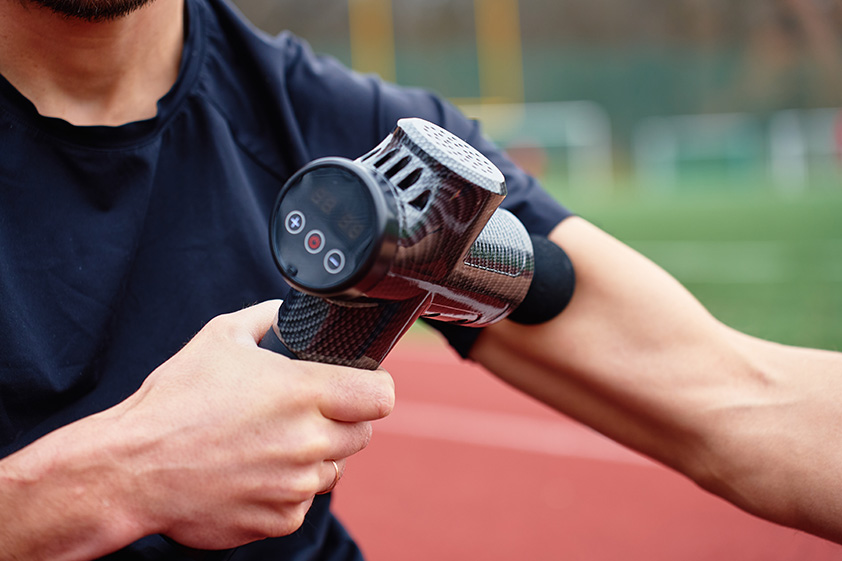 Athlete using a massage gun on the arm to relieve muscle tension and support sports recovery.