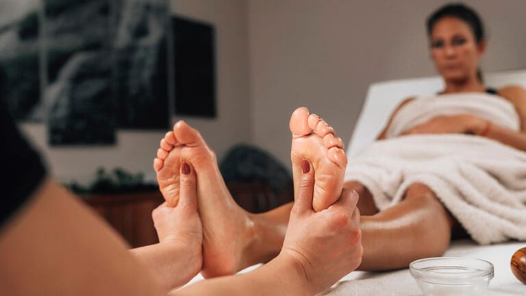 Reflexology practitioner applying pressure to foot reflex points often associated with relaxation and lower back comfort, sometimes explored by people with sciatica.