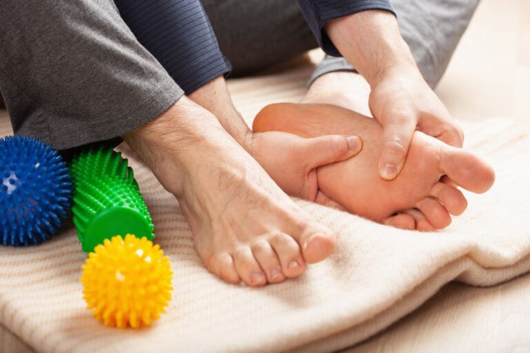 Person using their hands to apply pressure to reflex points on their own foot as part of a self-reflexology practice.