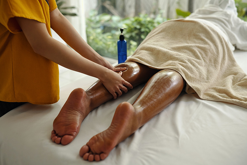 Therapist massaging an athlete’s legs with oil during a sports massage, where aromatherapy is used to support muscle relaxation and recovery.