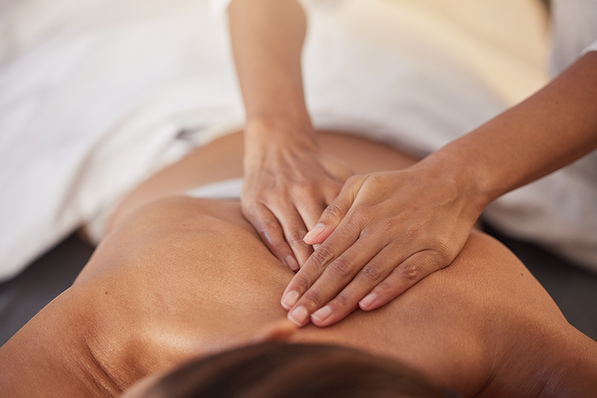 Massage therapist using gentle hand pressure on a woman’s back during a relaxing spa massage treatment.