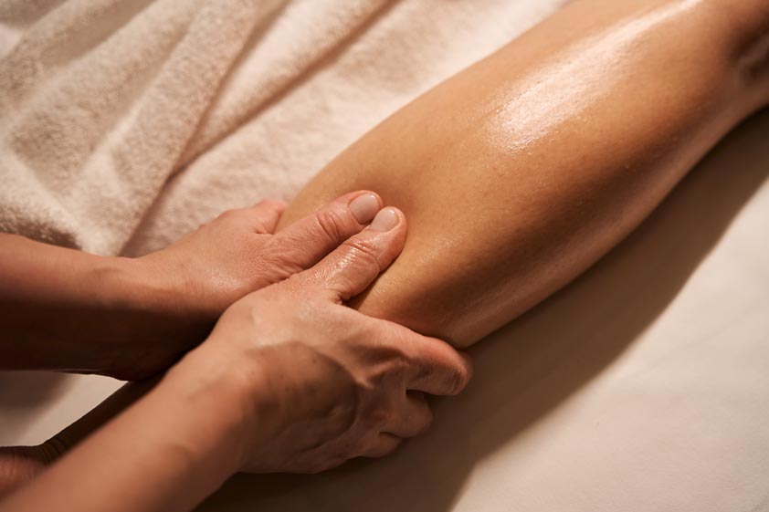 Reflexologist massaging acupoint on customer calf using thumbs