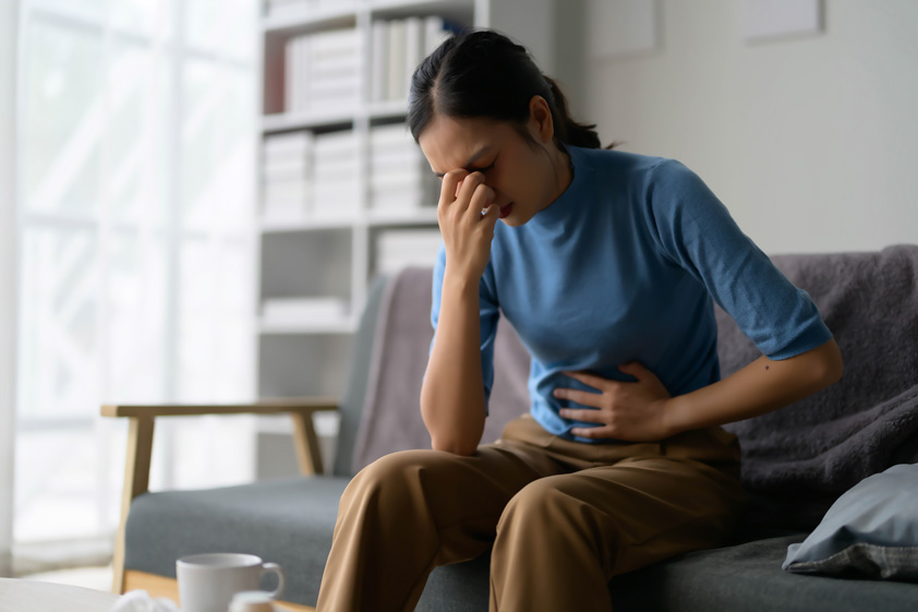 Woman Experiencing Abdominal Pain Sitting on Couch