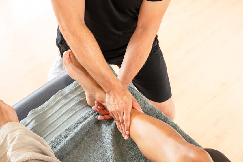 Sports massage therapist applying deep pressure to a client’s leg during a professional treatment session
