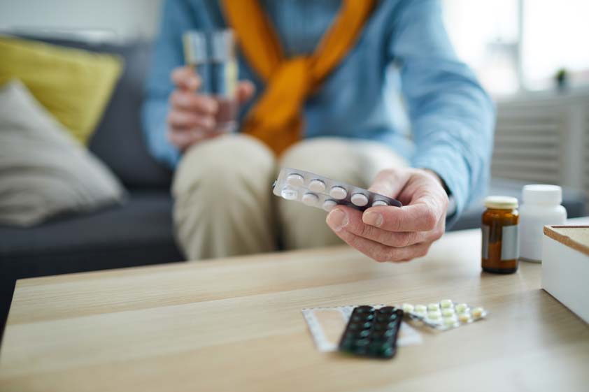 Man taking medication with water at home as part of preparing for a deep tissue massage appointment