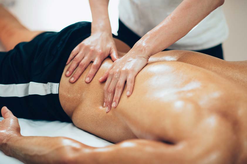 Sports massage therapist applying pressure to a man’s lower back during a workout recovery session.