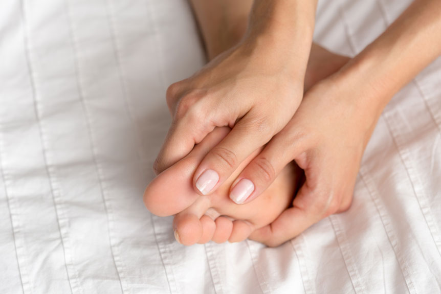 woman hands massaging foot on white bedding