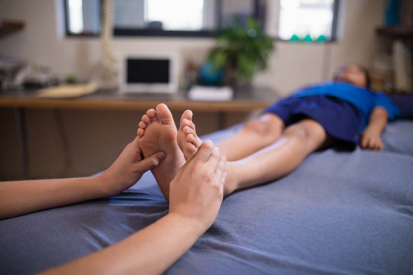 Boy lying on bed while receiving foot massage from female therapist