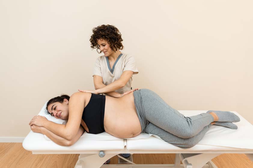 physiotherapist giving massages to the back of a pregnant woman lying on her side on a massage table